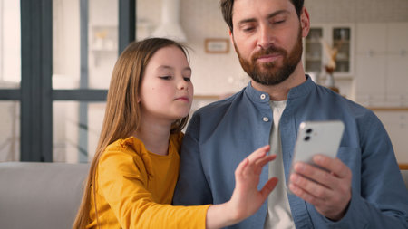 Glad Caucasian child little girl talking father male dad man using mobile phone typing play online game daughter kid scroll social media parent pay for purchase Internet smile home family cyberspaceの写真素材