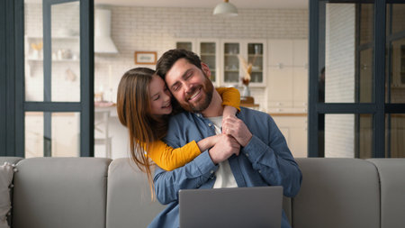 Laughing carefree Caucasian family cheerful little daughter kid hug distract dad father man from working laptop device hugging touching having fun at home girl child cuddle disturb bother male guy funの写真素材