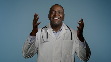 Hopeful african american man doctor ethnic male medical worker in studio blue background crosses...