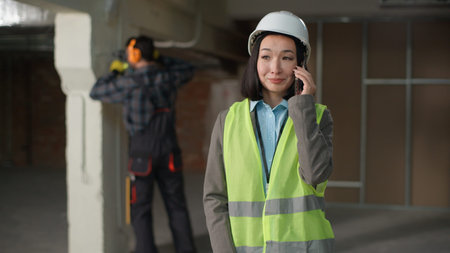 Happy multinational builders Asian woman engineer mobile phone call communication smartphone...