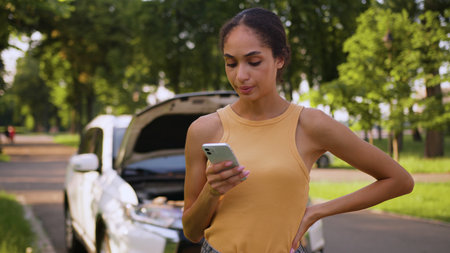Unhappy African American woman upset female businesswoman worried car driver breakdown auto texting chatting online mobile phone smartphone broke problem city transport stressed girl parking outdoorsの写真素材