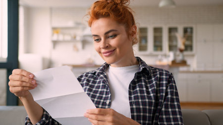 Caucasian woman female girl lady check correspondence checking open envelope reading letter read information bank clinic notification offer at home couch indoors mail credit loan insurance postalの写真素材