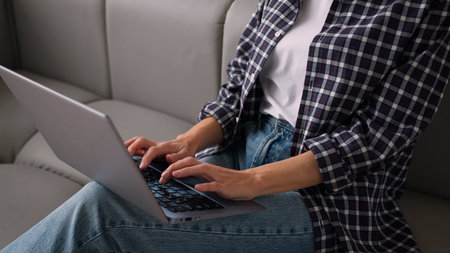 Cropped view unrecognizable Caucasian woman using laptop typing message unknown girl female hands chatting computer browsing surfing internet social media studying working online remote at home couchの写真素材