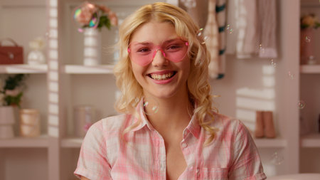 Caucasian teen girl woman female in candy pink home bathroom happy smiling laughing looking at camera putting on glasses in hearts shape laugh having fun joyful fooling flying soap bubbles glamourの写真素材