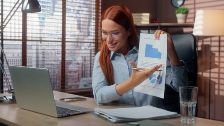 Caucasian businesswoman smiling happy talking video call laptop in office showing good results financial grows graphic data marketing success business woman girl female at table virtual consultationの写真素材