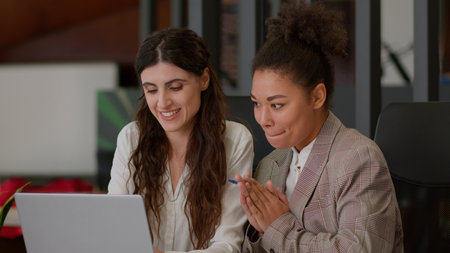 African American Caucasian female office coworkers happy cheerful girls ladies business partners businesswomen rejoice win online computer laptop screen multiracial women celebrate high fiveの写真素材