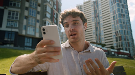 Caucasian man using mobile phone smartphone online meeting greeting waving headphones city male guy...
