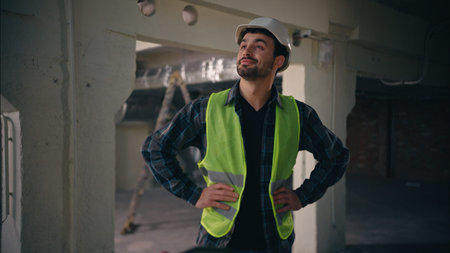 Happy proud Caucasian guy holding hands on hips in construction manufactory architect man technician...