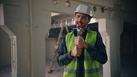 Cheerful active Caucasian man builder holding hammer working tool using as microphone singing song...