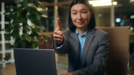 Asian Korean Chinese Japanese businesswoman typing using laptop computer online business woman female girl lady in office worker showing gesture thumb up approve good manager employer recommend likeの写真素材