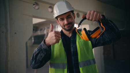 Cheerful Caucasian electrician man architect engineer smile builder technician guy showing earmuffs...