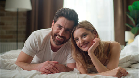 Carefree family glad Caucasian couple relaxing in bed looking at camera in bedroom pair wife husband...