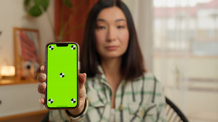 Serious Korean Japanese woman business businesswoman showing mobile phone green screen at camera chroma key portrait female Asian Chinese girl home indoors lady template mock up smartphone display appの写真素材