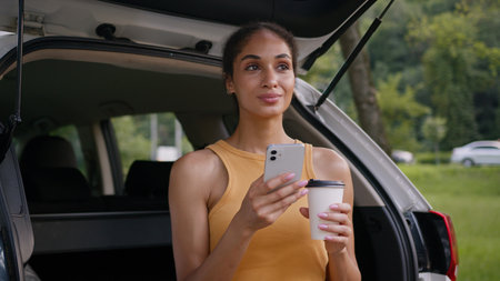 African American woman holding mobile phone smartphone chatting online trunk car auto automobile...
