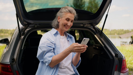 Happy retiree laughing Caucasian senior elderly business woman mature female businesswoman freelancer car auto driver user hold mobile phone texting app social media travelling laugh outside natureの写真素材