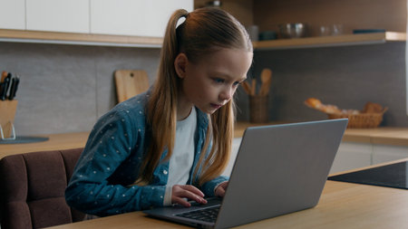Caucasian girl child kid daughter at home kitchen looking at screen monitor of laptop online...