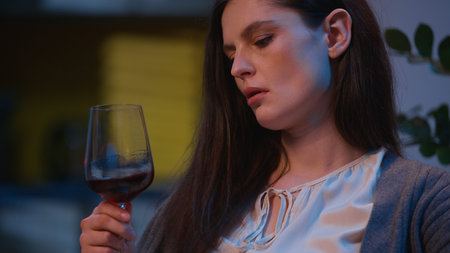 Sad woman at home night drink glass of wine alone watching photo album memories looking pictures thoughtful pensive female Caucasian girl relaxing upset drunk addict alcohol problem depression eveningの写真素材