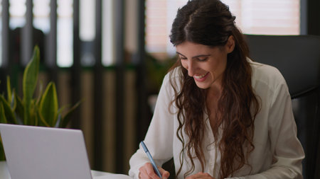 Smiling happy Caucasian woman business worker office manager girl female lady businesswoman planner online studying class learn exam course video call laptop conference chat write notes notebook tasksの写真素材