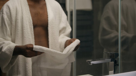 Man after shower naked African American male wearing bathrobe posing bathroom hotel spa looking mirror reflection smiling happy guy morning beauty procedure washing body hygiene routine health careの写真素材