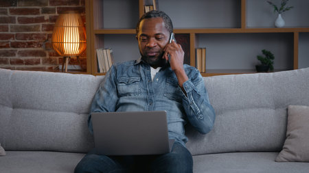 Happy African American man male guy freelancer businessman working with laptop talking mobile phone...