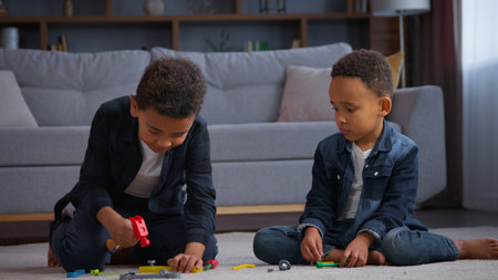 Two African American children playing with plastic toys at home brothers ethnic kids sons boys siblings friends play game repair on floor building with hammer friendship family childhood playtimeの写真素材