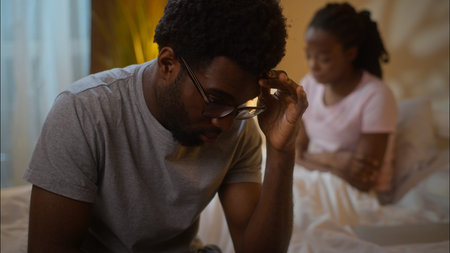 Sad upset African American man boyfriend sitting bed think unhappy offended woman girlfriend breakup...