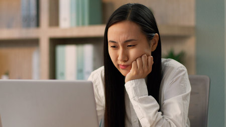 Upset unhappy disappointed Asian Japanese businesswoman female Korean Chinese ethnic business woman secretary office worker looking laptop computer bad connection error working fail losing bet indoorの写真素材