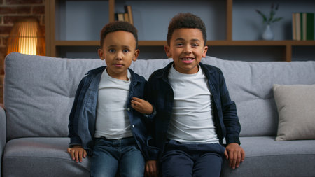 Two funny African American children greeting hello at home happy carefree boys kids siblings brothers sons in living room together looking at camera waving hands video call family joy fun childhoodの写真素材