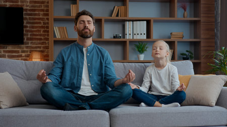 Happy Caucasian family meditation at home father with little daughter meditate together on couch dad with cute funny adorable kid child girl meditating breathing exercise calm peace pause wellnessの写真素材