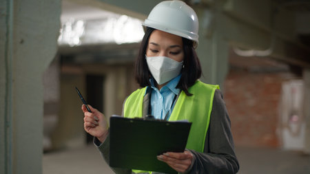 Asian Japanese woman builder in safety mask hold tablet pointing counting checking building plan businesswoman Korean Chinese contractor business female girl architect engineer document constructionの写真素材