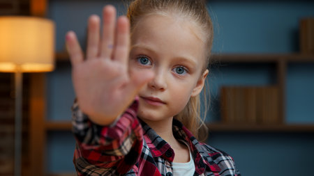 Portrait Caucasian confident little girl child kid daughter showing stop gesture holding hand in front no keep distance sign deny forbidden arm looking at camera in evening home protection reject notの写真素材