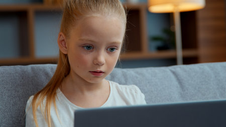 Caucasian child girl typing laptop at home focused little kid daughter pupil schoolgirl user studying with computer distant education playing at cyberspace communicate in internet chatの写真素材