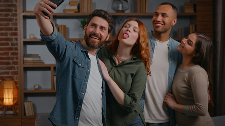 Funny four multiracial friends make selfie photo together posing grimacing smiling happy cuddling photographing recording video on mobile phone diversity people at home party men women take pictureの写真素材
