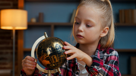 Cute clever little Caucasian child kid girl daughter spinning gold globe studying at evening home junior schoolgirl exploring world search countries learning study dreaming trip traveling conceptの写真素材