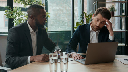 Two diverse business men team upset with bad result businessmen workers multiracial partners in office difficulty trouble with papers and laptop failure low stats displeased working meeting teamworkの写真素材