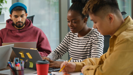 Three multiracial casual informal business employers at table indoors in corporate office looking in documents review data diagram laptop use startup development team busy concentrated workgroup workの写真素材