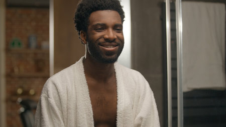 African American man looking at mirror reflection hotel bathroom smiling bearded guy shaving beard lotion gel cream soft skin shave face grooming morning hygiene male cosmetics facial care moisturizeの写真素材