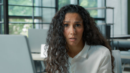 Close-up confused Hispanic business woman looking at camera shrug shoulders with computer businesswoman puzzled reading bad news email notification ethnic female girl worried with network in officeの写真素材