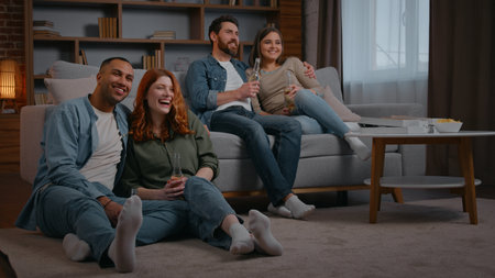 Carefree multiethnic four friends having fun watching tv at home party double date two couples watch television talking men laughing smiling women enjoying cinema movie film program friendship holidayの写真素材