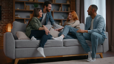 Happy four multiethnic friends at home party on couch talking carefree group of multiracial diversity people men women laughing having fun together discussing at apartment meeting chatting friendlyの写真素材