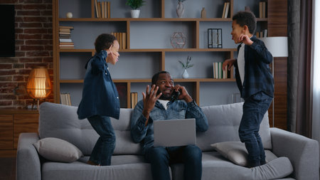 African American family father work noisy kids jump on couch dad with laptop talking mobile phone annoyed busy near two children sons little boys jumping on sofa parenthood trouble stressの写真素材