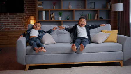 Happy African American little boys jumping on couch joyful positive ethnic children carefree active...