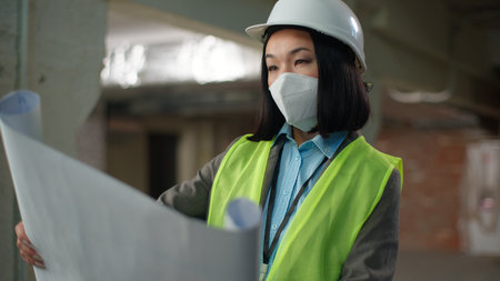 Asian Korean Chinese Japanese woman builder looking check construction plan building project blueprint female inspector girl nod head engineer architect foreman in hard hat safety mask industry workerの写真素材