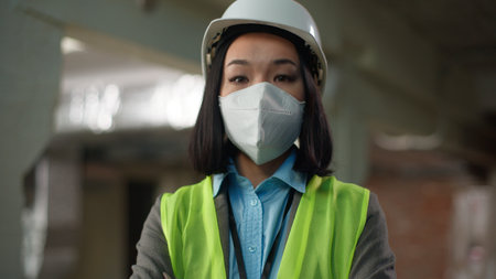 Confident Asian Korean Japanese woman looking at camera crossed hands posing portrait female builder in safety mask businesswoman business Chinese girl in industrial building architect engineer workerの写真素材