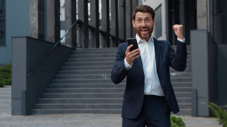 Happy excited Caucasian mature business man successful win with phone in city yelling happy winner middle-aged businessman male entrepreneur winning with mobile smartphone app reading good news gladの写真素材