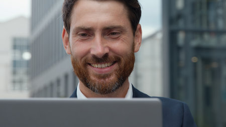 Close-up smiling handsome mature Caucasian business man looking at laptop in city smile toothy happy businessman male look at computer screen happy surfing internet outdoors in downtown working in netの写真素材