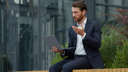 Professional Caucasian mature business man talking video call with laptop in city consultant businessman male sitting outdoors communicating with computer conference virtual speaking talk consultingの写真素材