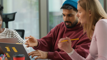 Pensive thinking Arabian informal business man Indian male worker startup founder working with laptop typing writing notes in office casual businessman job concentrated with two multiracial womenの写真素材