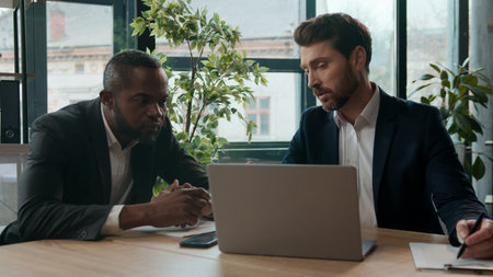 Multinational business team cooperation in office African American Caucasian businessmen corporate men teamwork man listening man consultant checking stats in document two diverse managers laptop workの写真素材