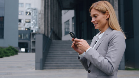 Smiling concentrated Caucasian adult business woman looking phone walking in city businesswoman internet addict scrolling social media mobile app female executive walk in downtown holding smartphoneの写真素材